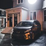 A minivan parked outside a well-lit house at night, creating a warm ambiance.