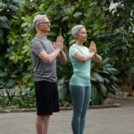 Senior couple practicing yoga poses together in a lush greenhouse setting.